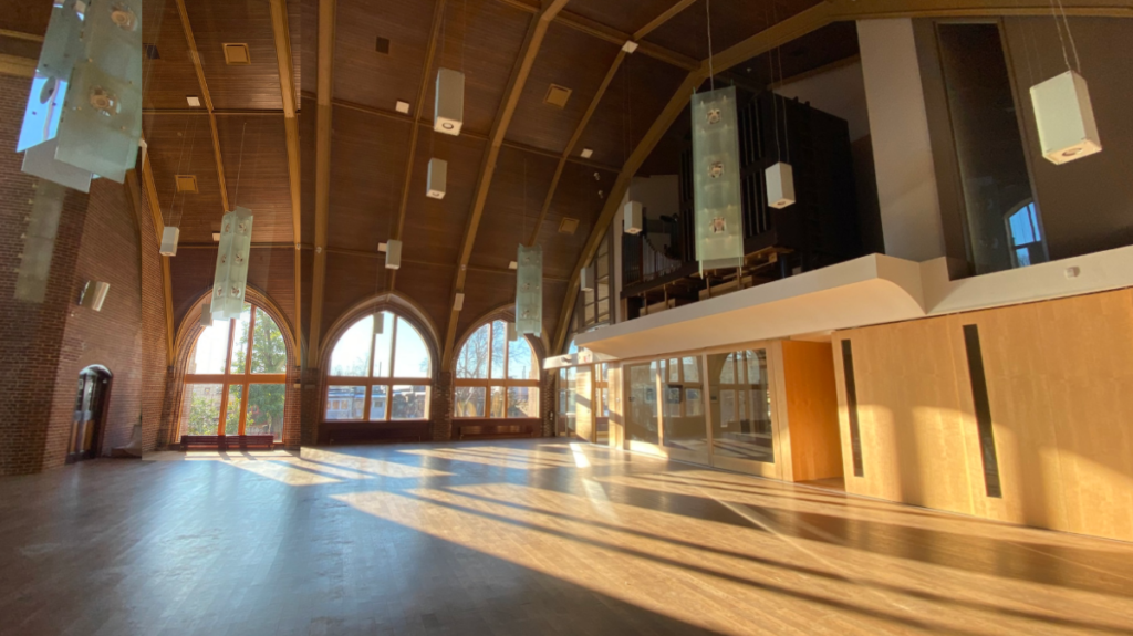 Bright, sunlit interior of Beach United Church main hall with large arched windows and warm wood ceiling