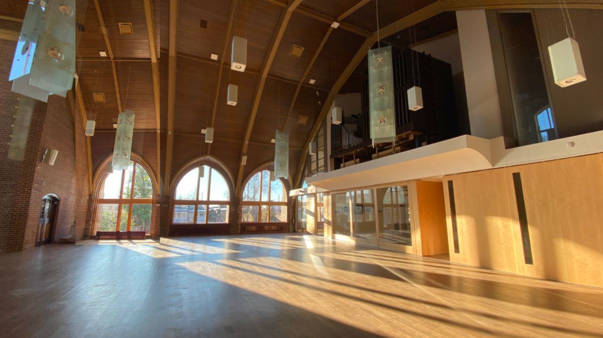 Bright, sunlit interior of Beach United Church main hall with large arched windows and warm wood ceiling